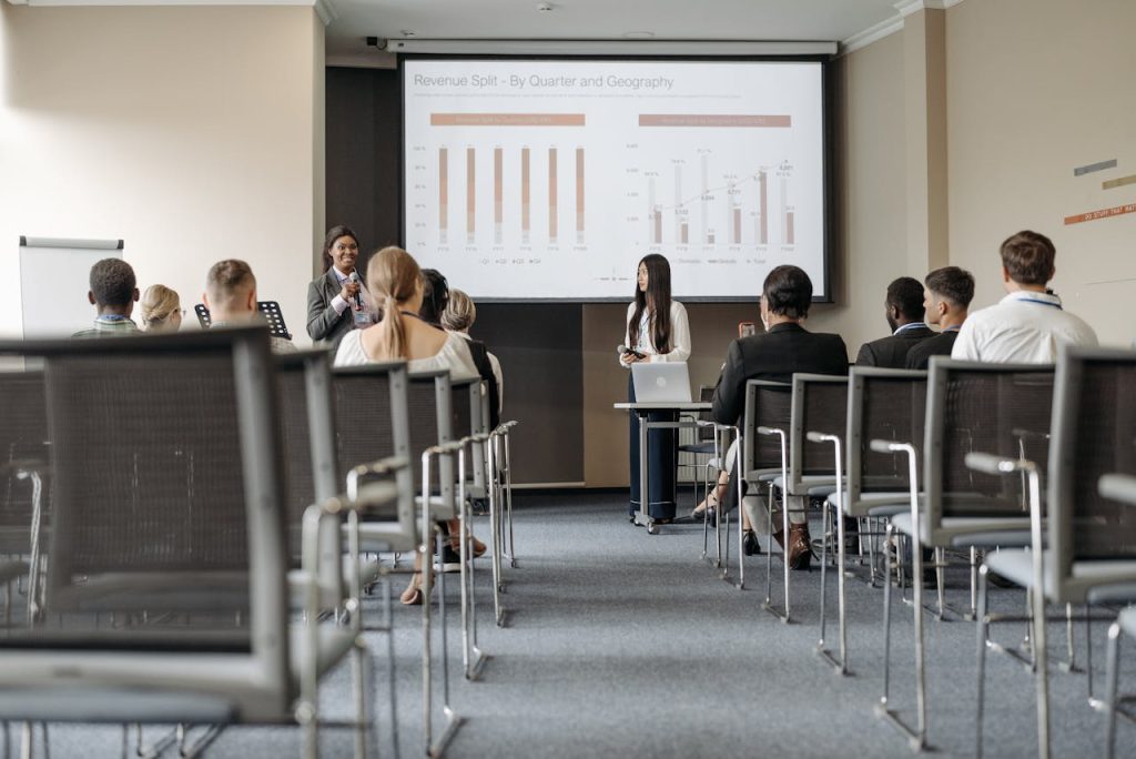 Business conference attendees listen to a presentation on revenue split by quarter and geography.